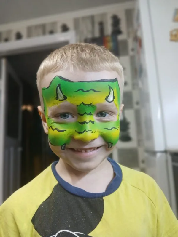 Child with green and yellow dragon face paint